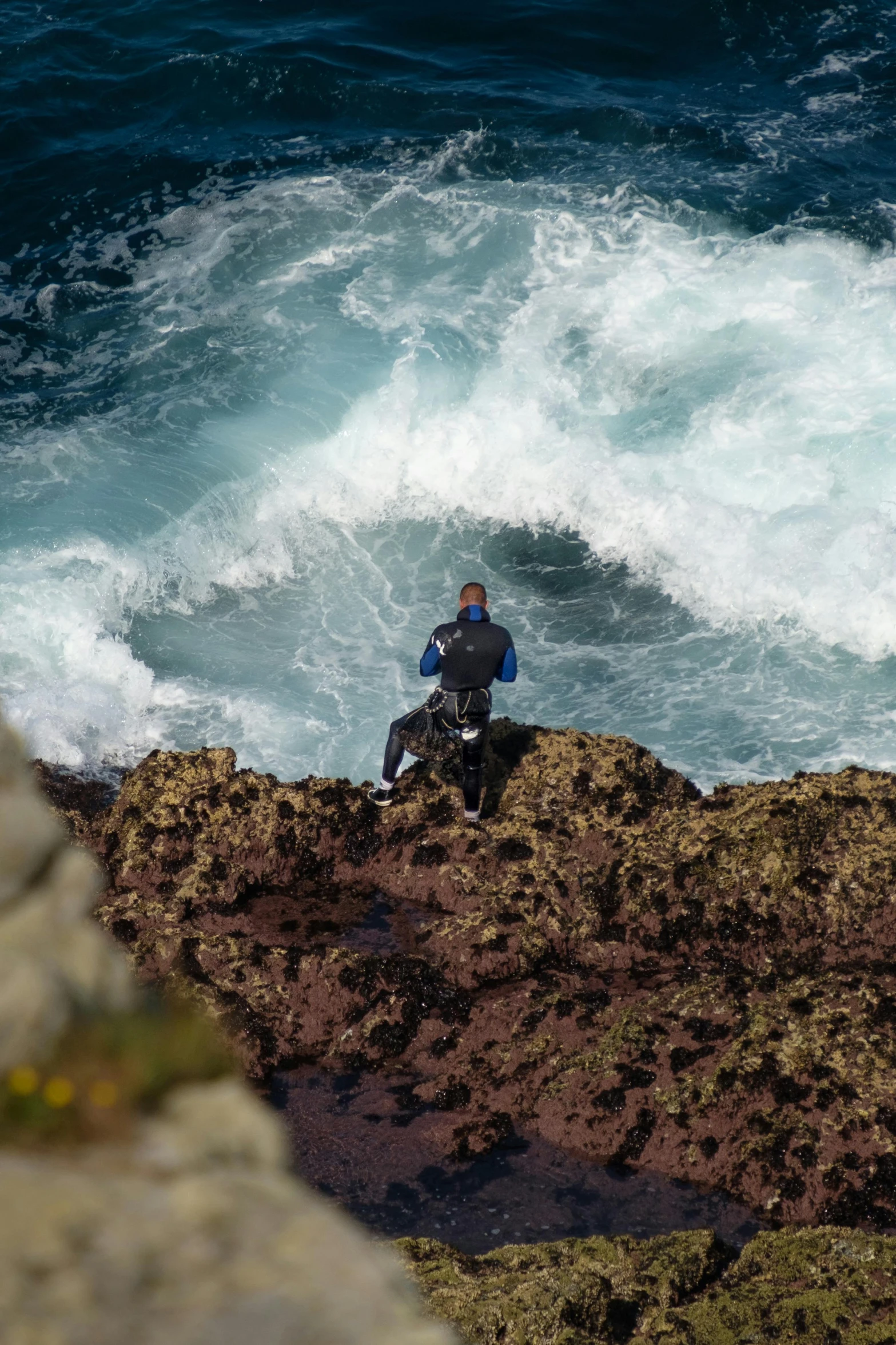 a man is sitting on the edge of a rock near water