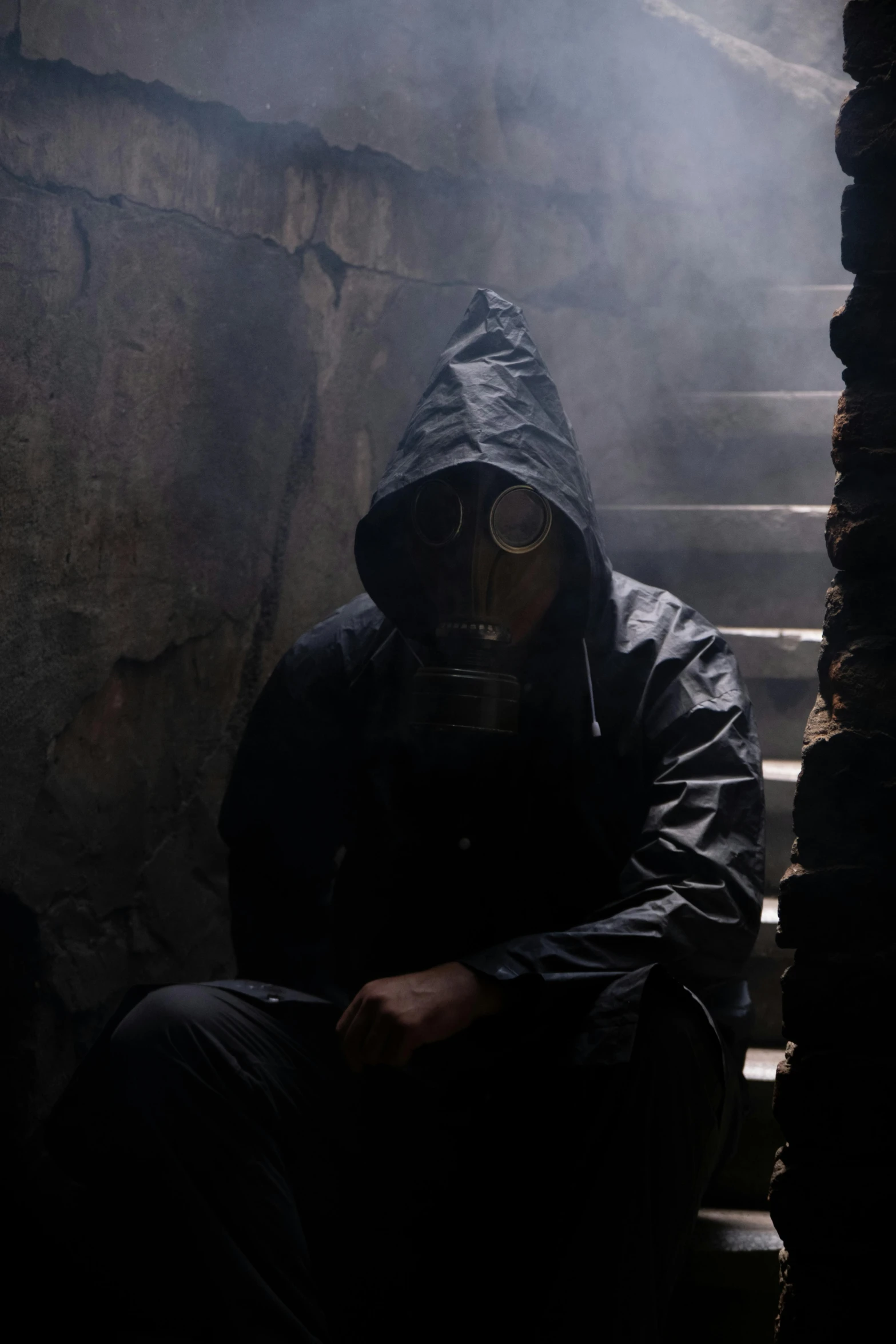 a man in a hooded jacket and gas mask sitting on a stair case