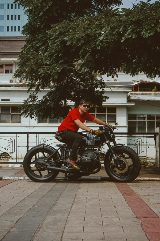 a man sits on his motorcycle under a tree