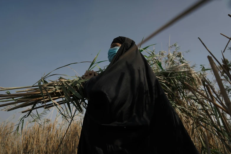 a woman wearing a surgical mask walking through a dry field