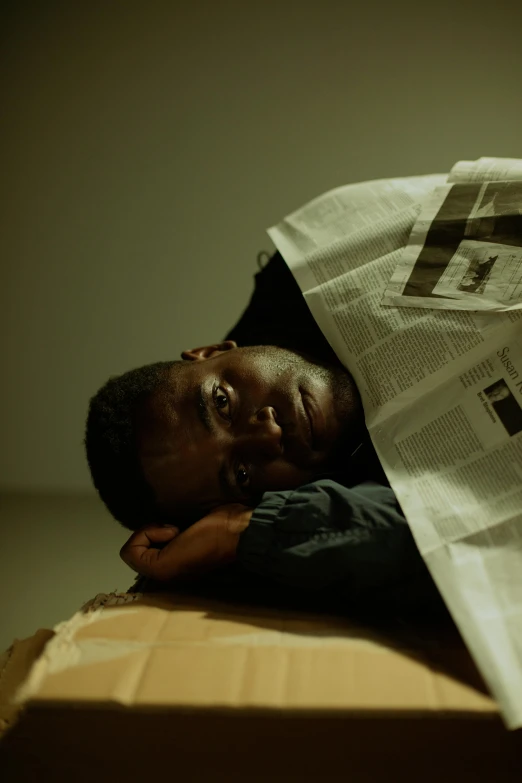 a person lying on top of a cardboard box while reading a newspaper