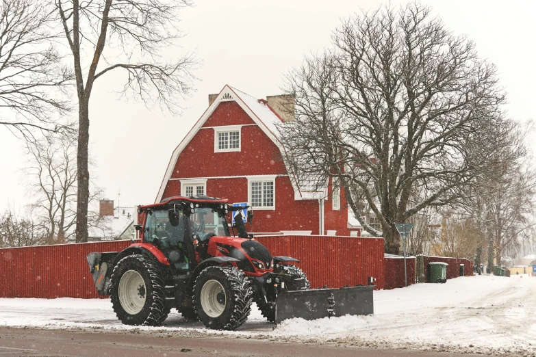 a tractor plowing a snow covered road near a house