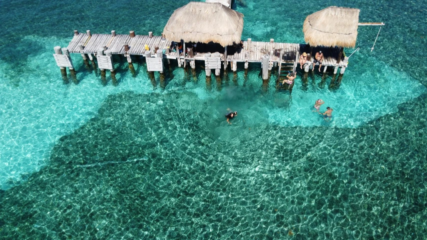 two people in the water with two thatched huts on a wooden pier