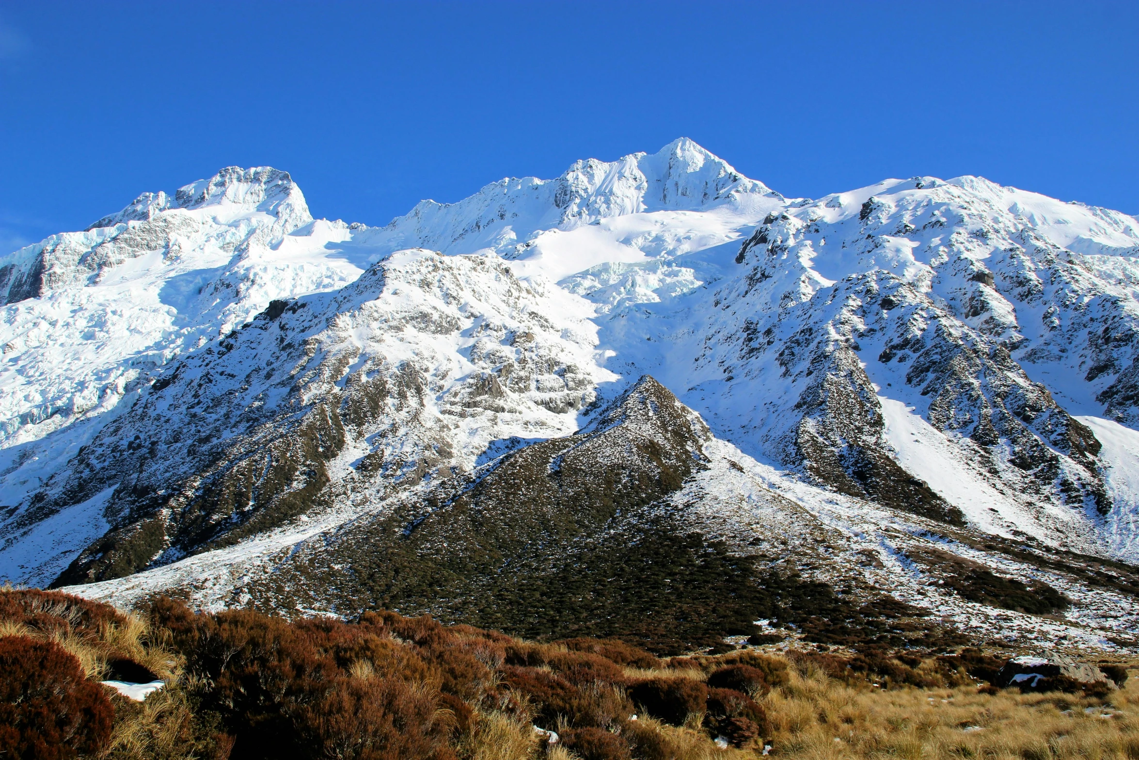 mountains covered in snow, with green grass on the bottom