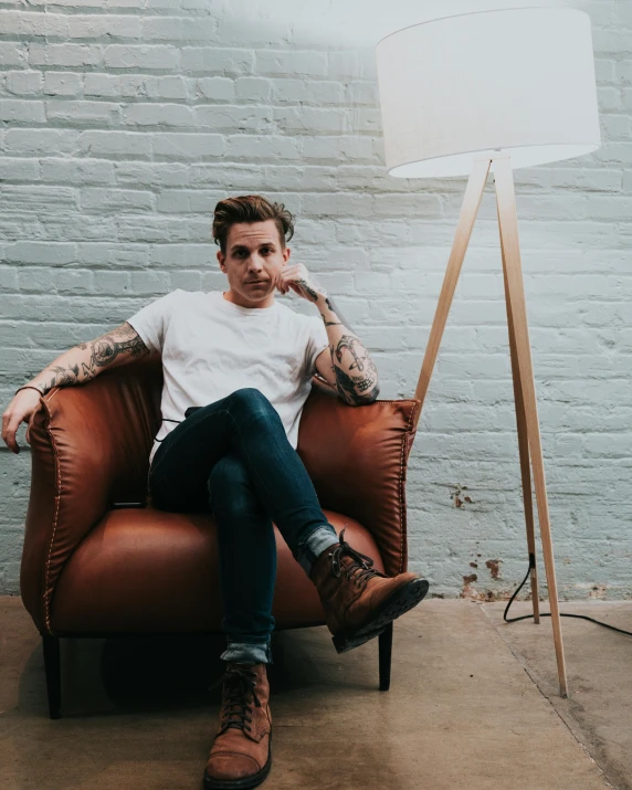 man with tattooed arms sitting on couch next to a lamp