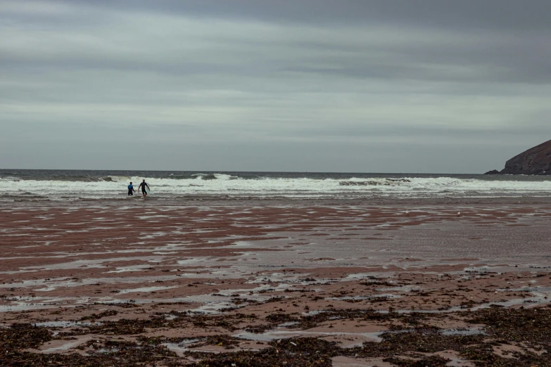 three people walk along an empty beach with a body of water in the distance