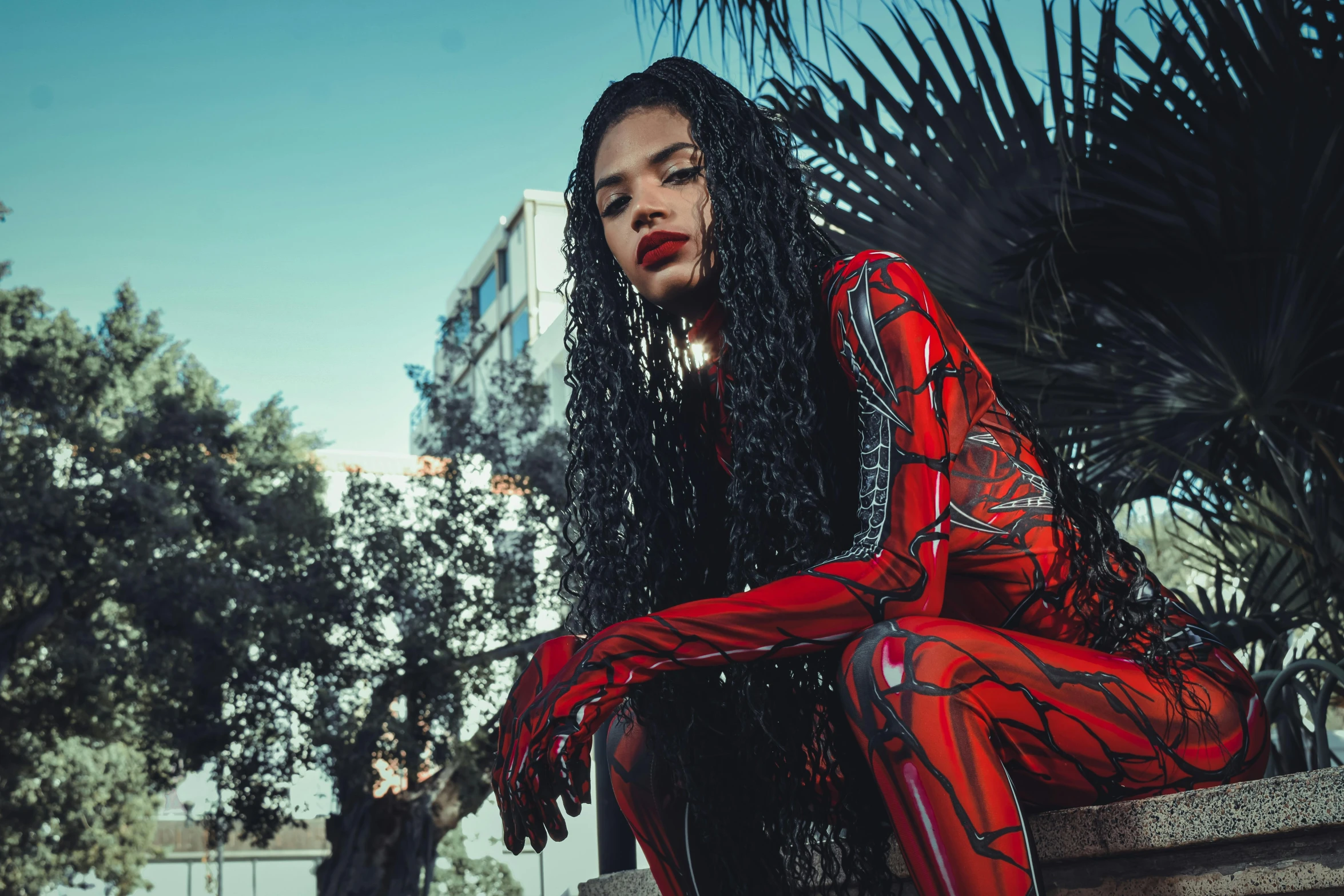 a woman is wearing a red body suit and sitting on a cement surface