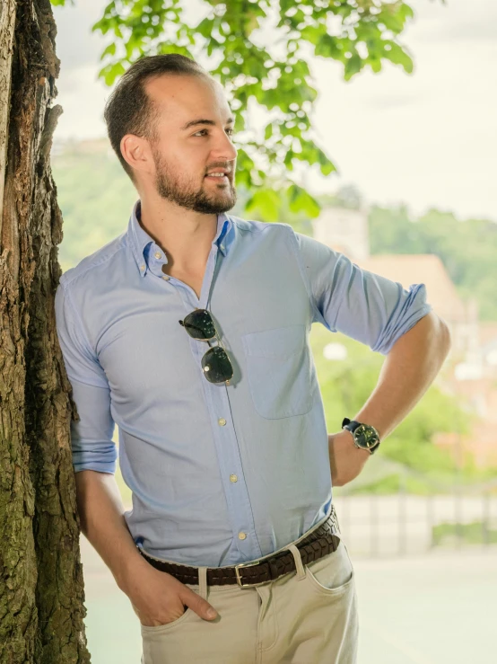 man standing next to tree with sunglasses on his neck