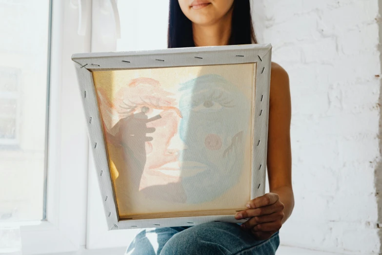 woman holding up framed painting on a canvas in a room