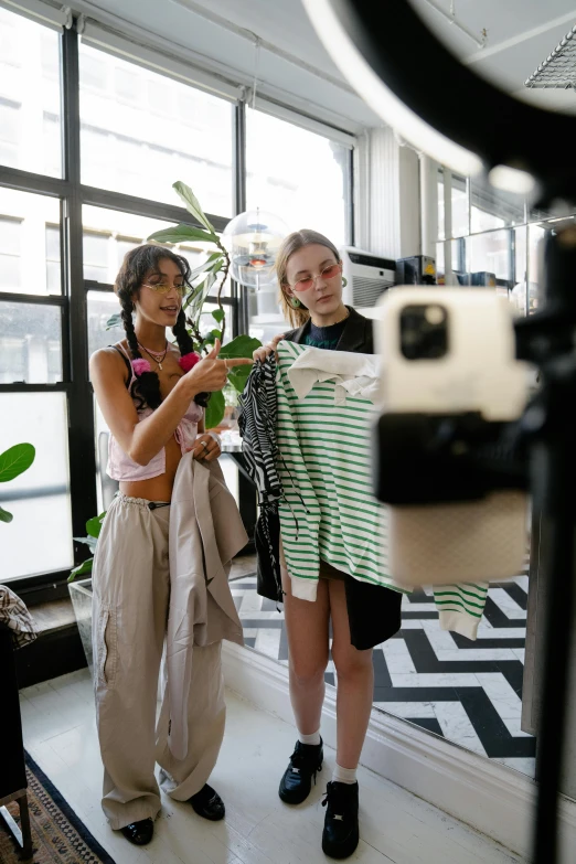 two girls stand side by side, while one girl is taking a picture with her camera