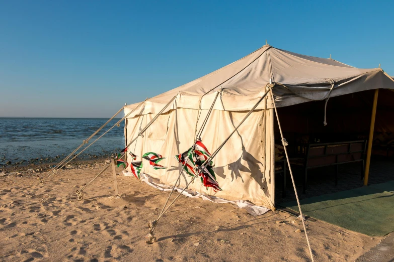 an off - grid canvas tent sits on the sand near the water