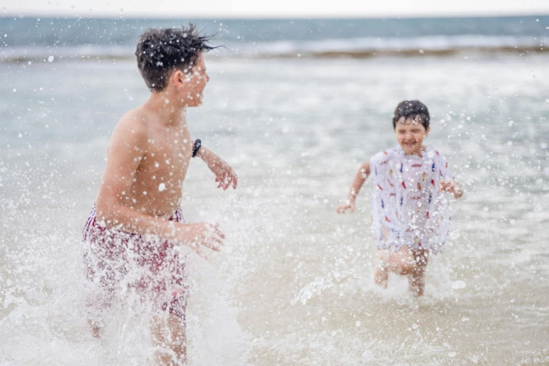 two young men running through water on a beach