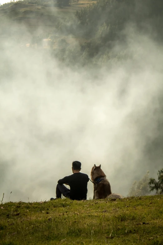 two people are sitting with their dog on a grassy hill