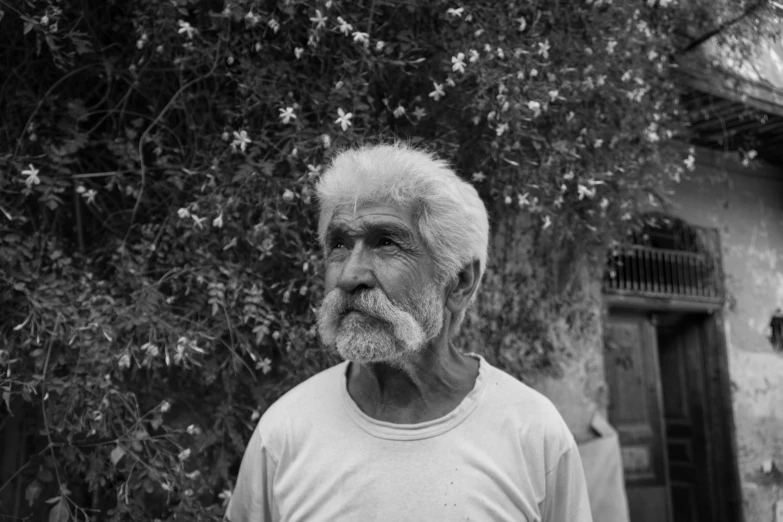 an old man with white hair and long hair, standing in front of a building