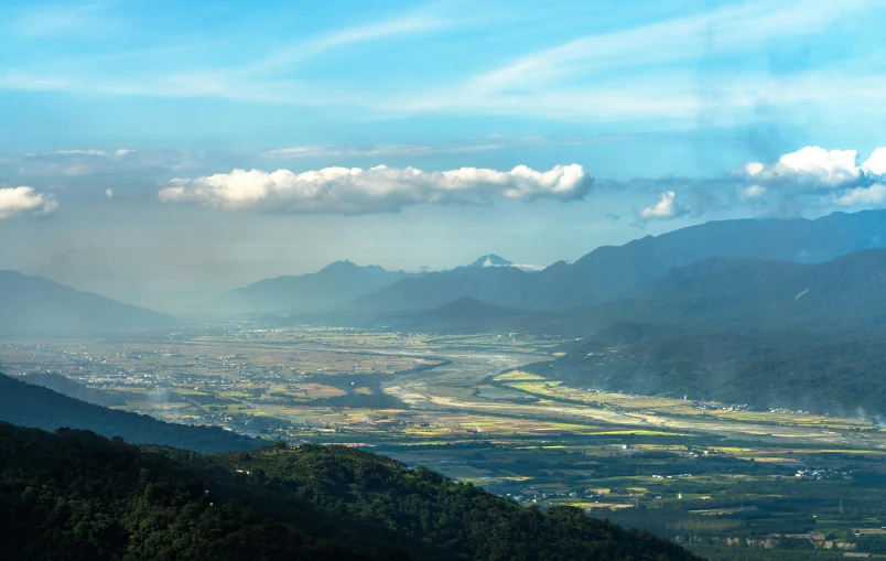 a view of a valley near mountains under blue skies