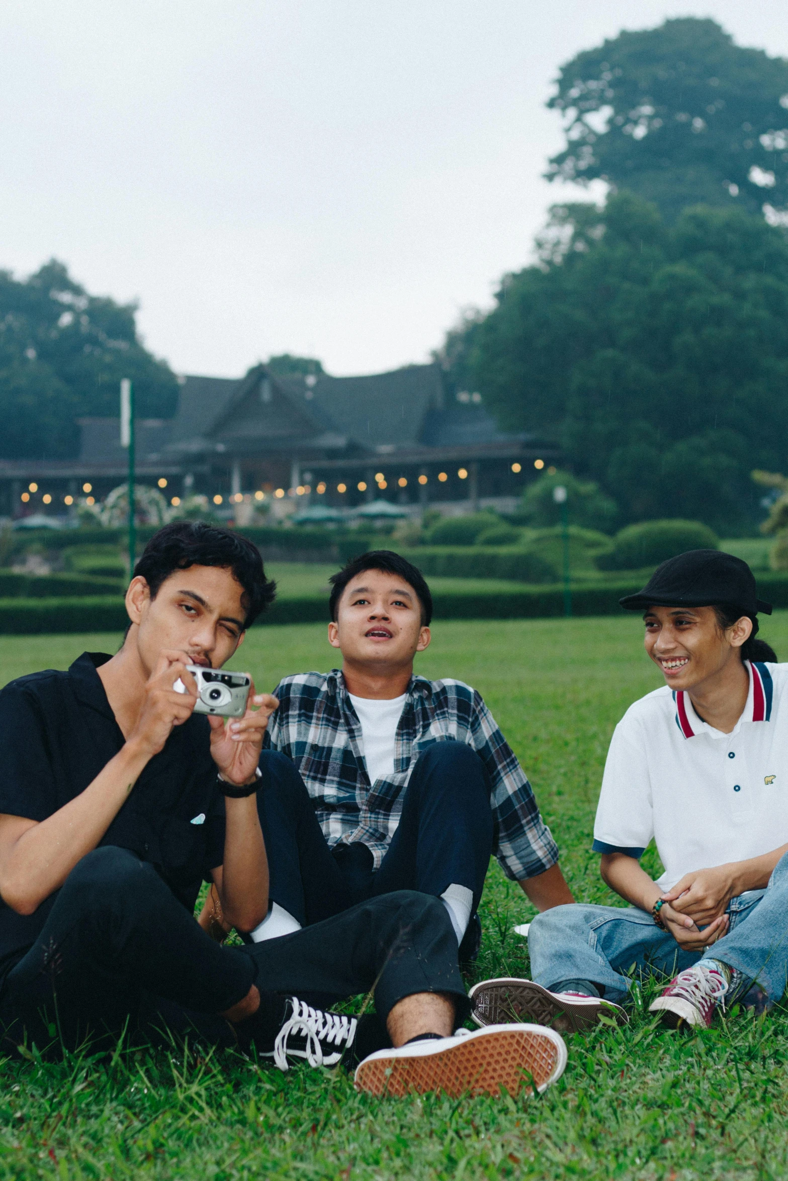 three young men sitting on the ground, one man taking a selfie