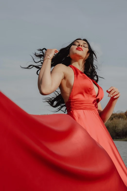 woman with flowing red dress posing near water