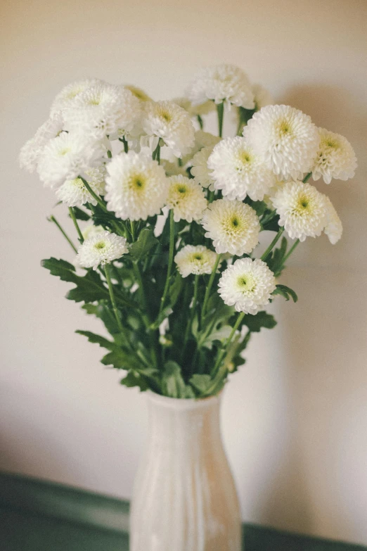 the white bouquet is in the vase with green leaves