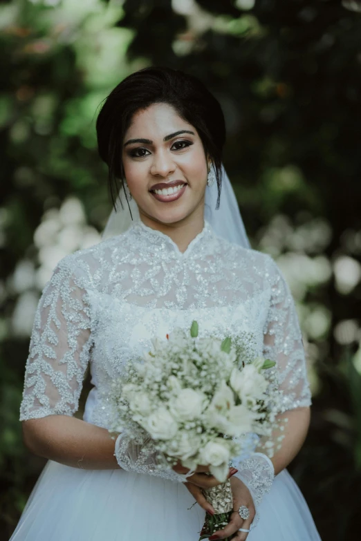 a bride standing in front of trees and smiling at the camera