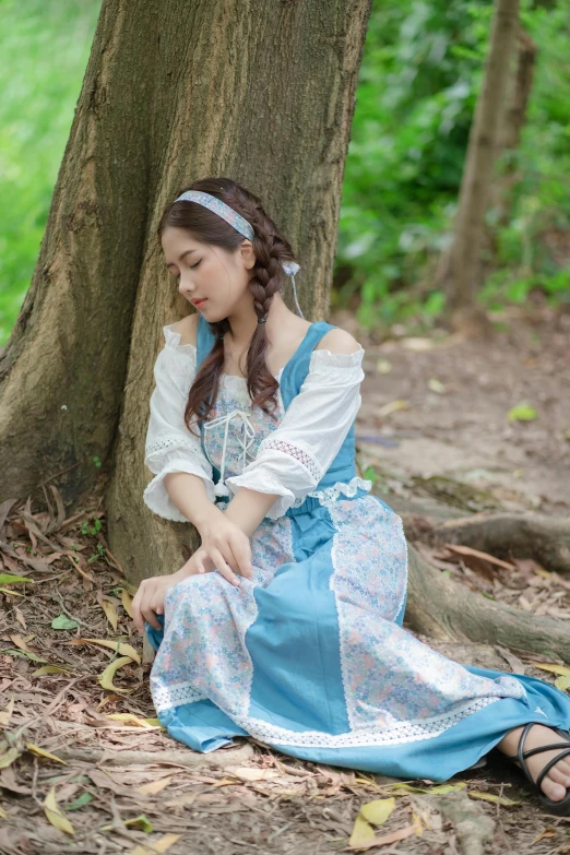 a  dressed in blue and white sitting against a tree