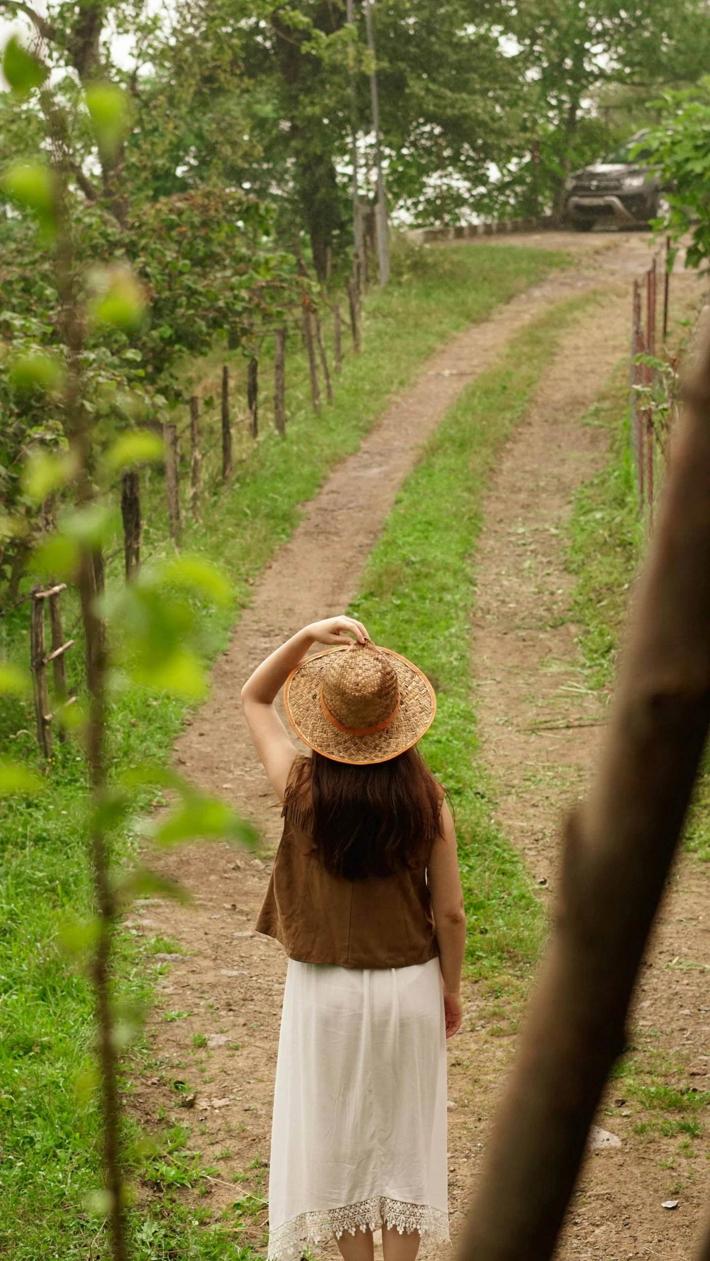 a woman in a hat walks down a dirt road