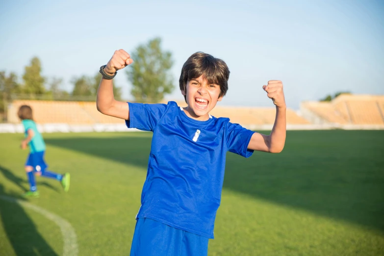 a boy in a blue shirt is raising his arms and smiling