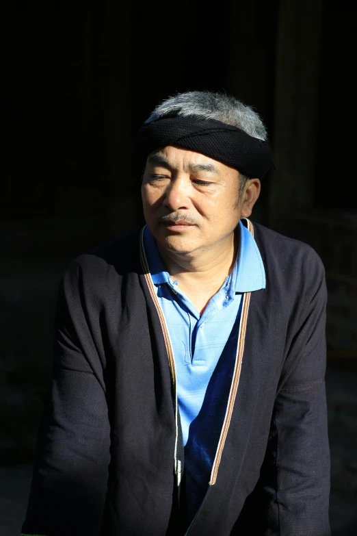 a man sitting outside wearing a blue shirt and black hat