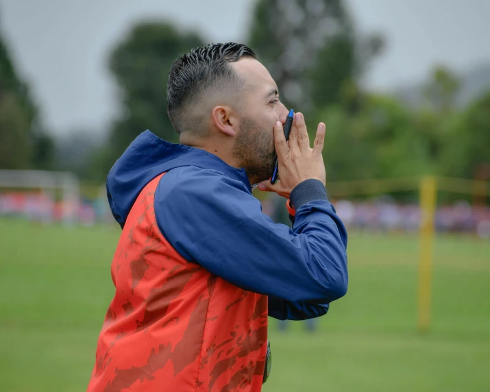 a man wearing an orange and blue vest is putting his finger under his nose while standing in the middle of a soccer field