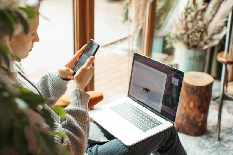 a person is holding a cellphone while using their laptop