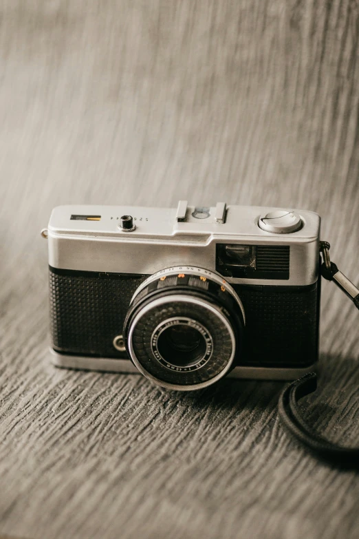 an old camera sitting on a wooden surface with an empty strap