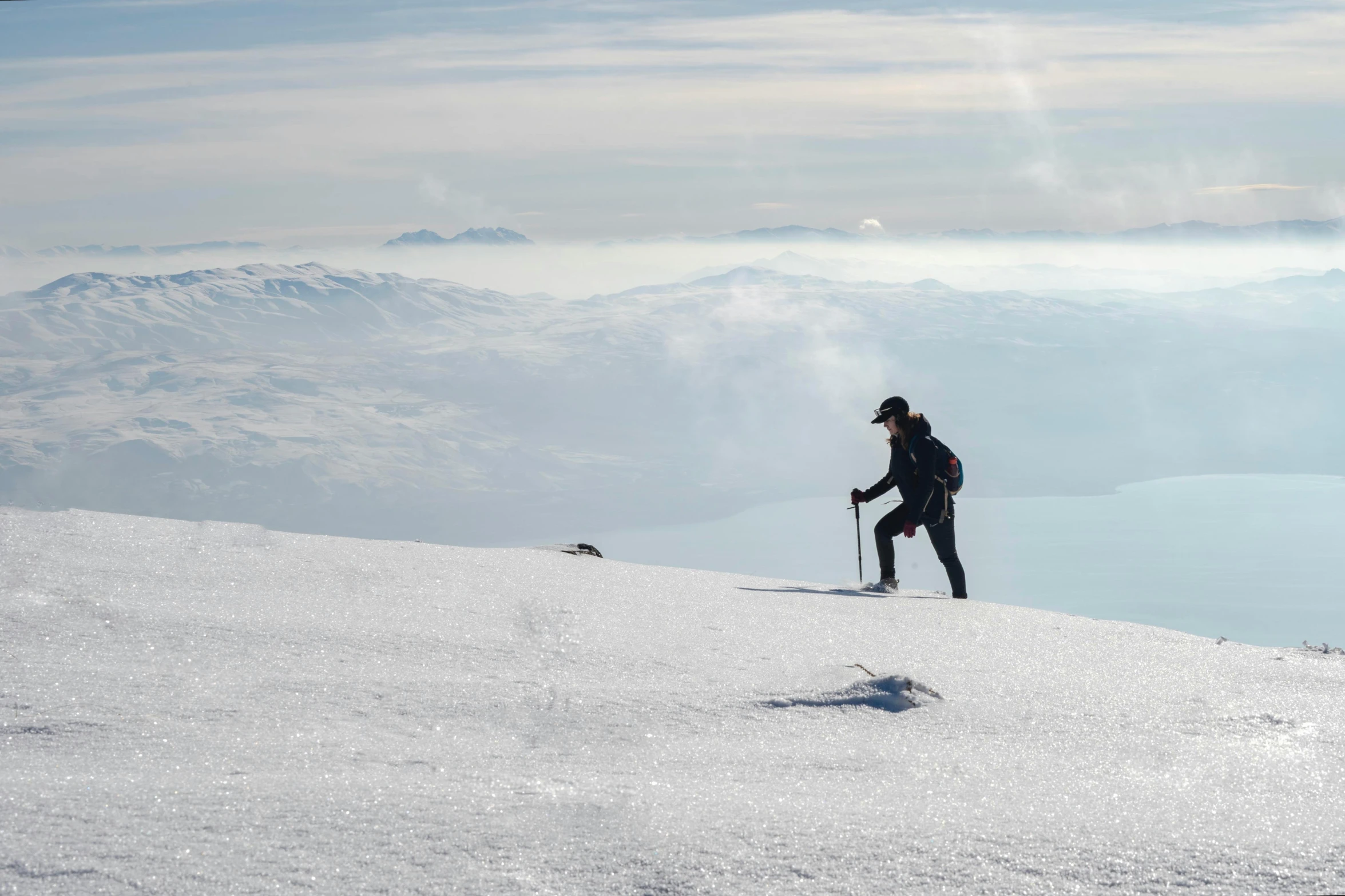 a snowboarder stands atop a snowy mountain with a view of the valley below