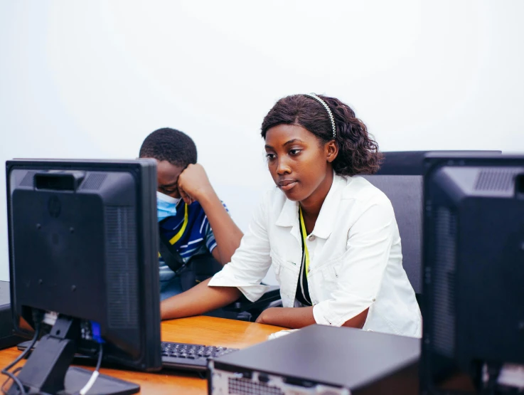 two people sit at computers with head phones on their heads