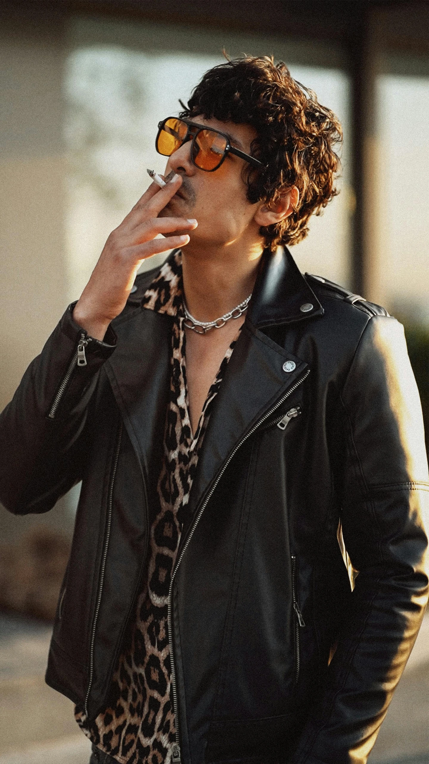 a person standing wearing a jacket, sunglasses and smoking a cigarette