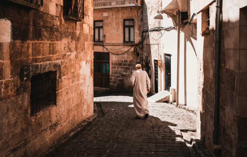 a man wearing a robe walks down an alley