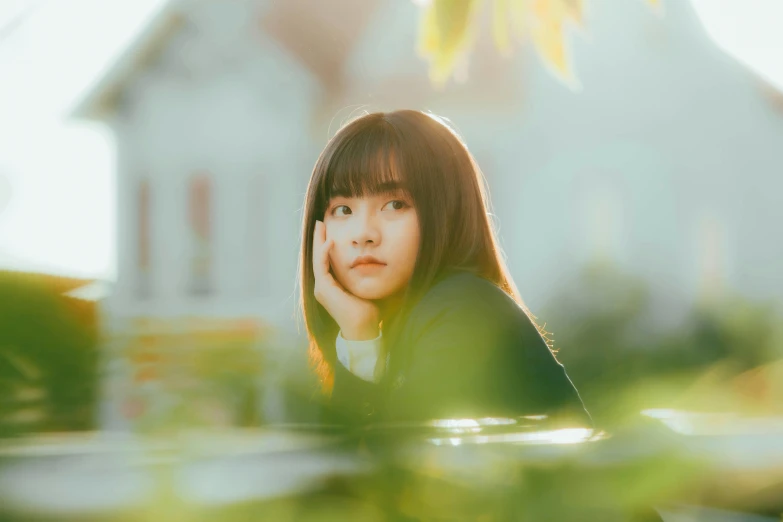 a girl sitting in a park looking to the right with a house in the background