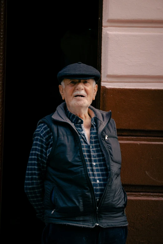 an elderly man with a cap and a vest standing in the doorway