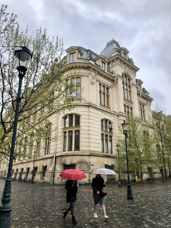 two people walking in front of a building under umbrellas