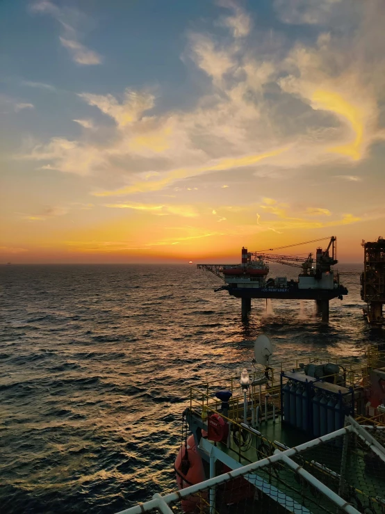 a sunset over the ocean with an oil platform in the background