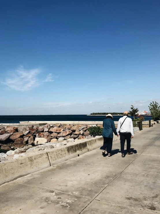 two people are walking along a road by the beach