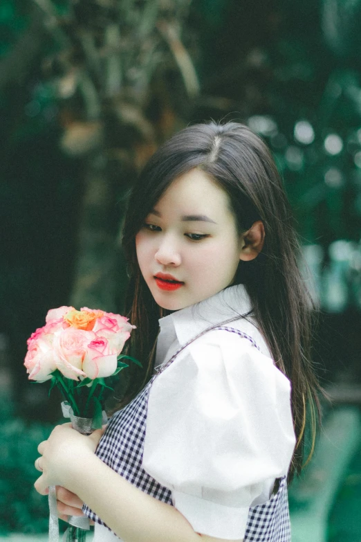 a girl standing in front of a tree and holding a pink rose