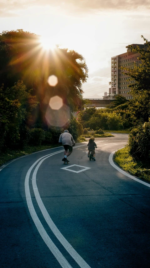 two people riding bikes down the street in the sun