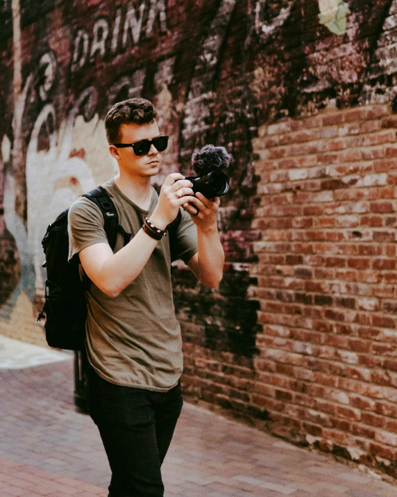 a man in glasses walks down the sidewalk with a camera