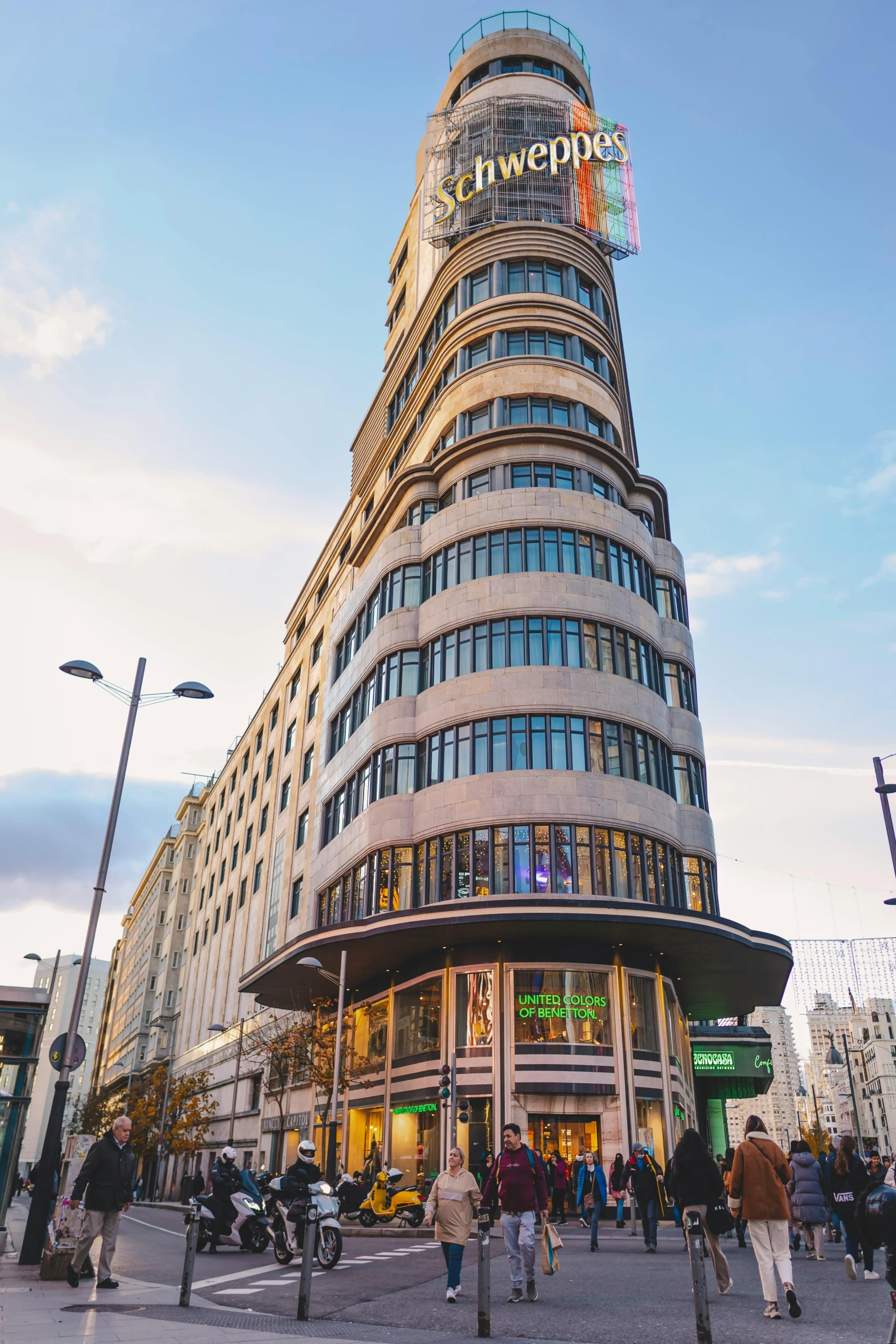 people gather outside a tall building that is surrounded by buildings