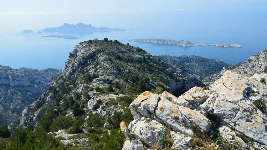 the view from a rocky hill shows the mountains with large rocks in the foreground and a body of water that lies out of sight