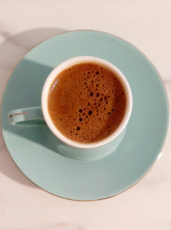 a plate holding a cup of coffee with foamy coffee inside it