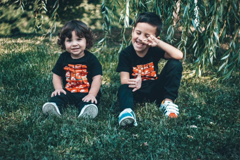 two children pose in the grass near some willow nches