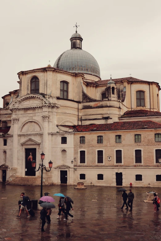 several people walking around an old building on a rainy day