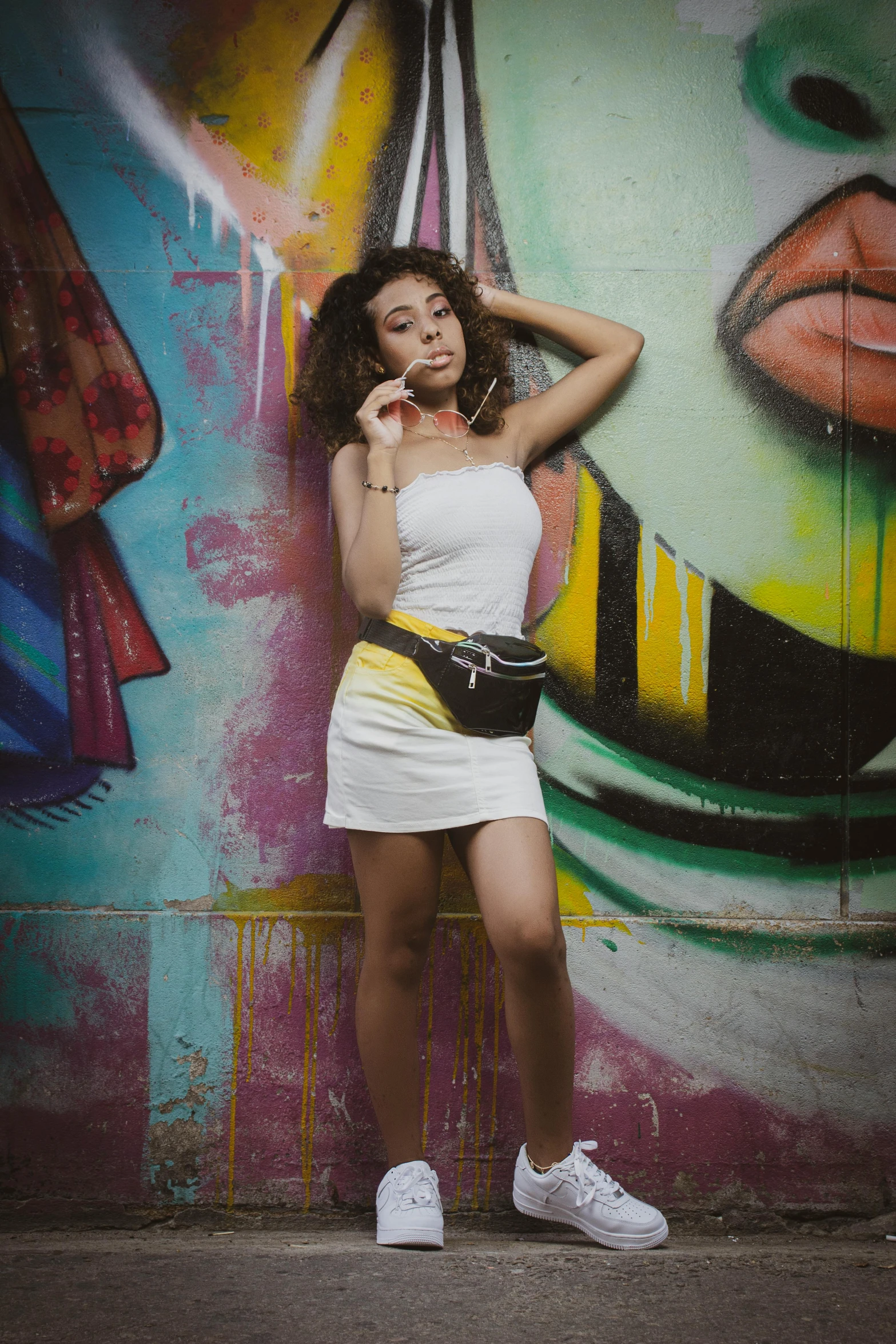 a woman wearing a dress leaning against a graffiti wall