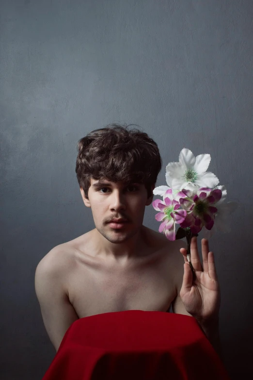 a man in red cloak holding flower and looking shirtless