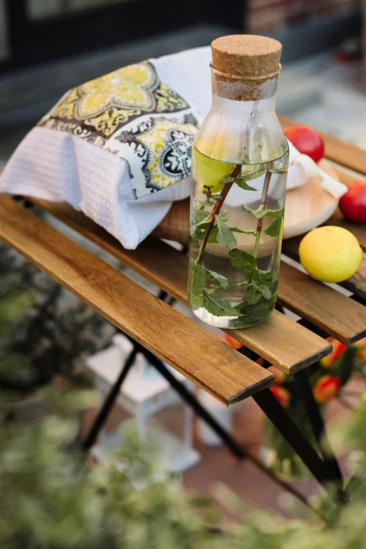 an old wooden bench with a bottle of water and lemon, apple, lime, tomatoes and oranges on it
